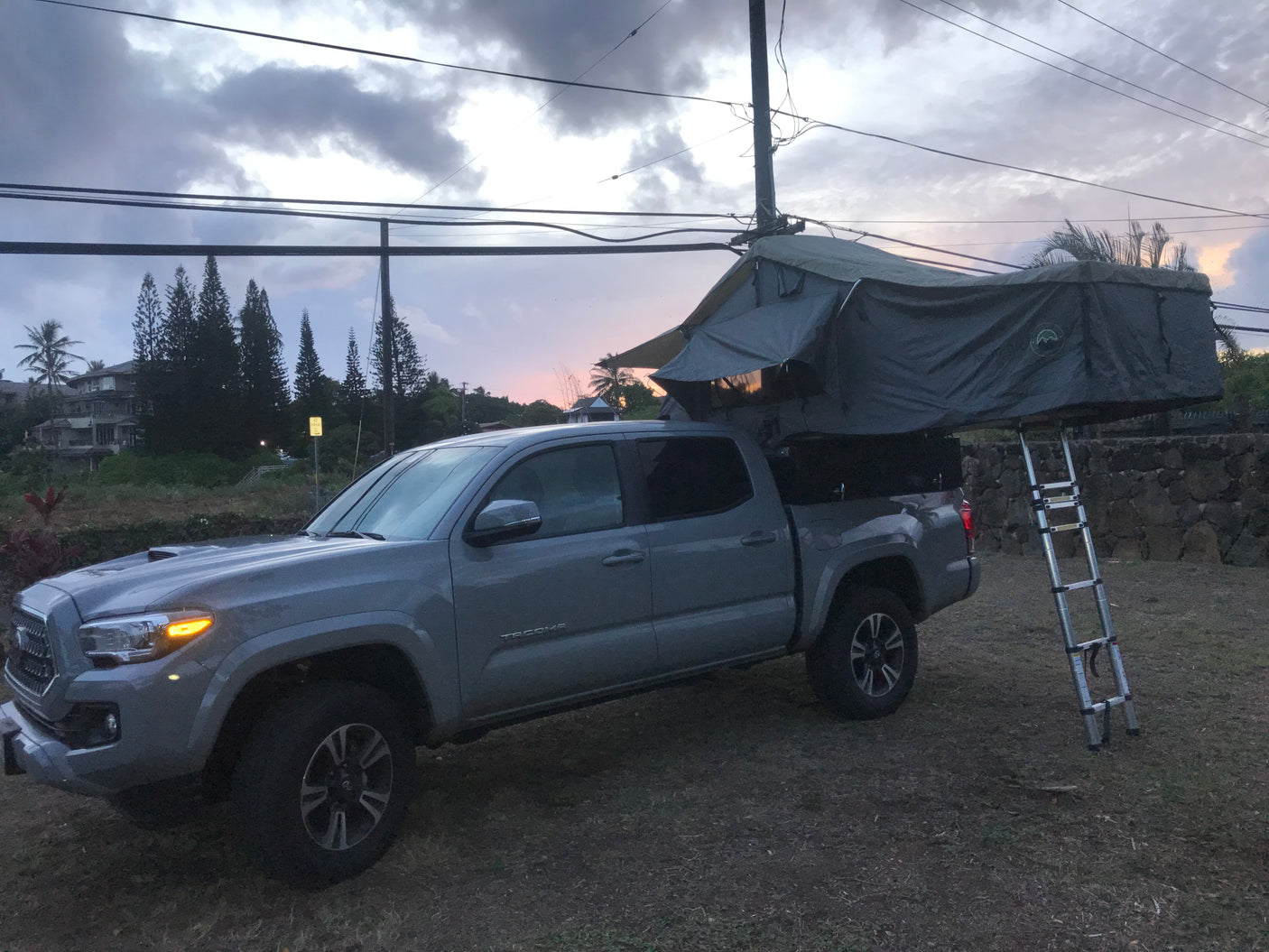 Experience truck camping! This grey pickup with a deployed roof-top tent is a unique alternative to an rv rental for outdoor travel at dusk.