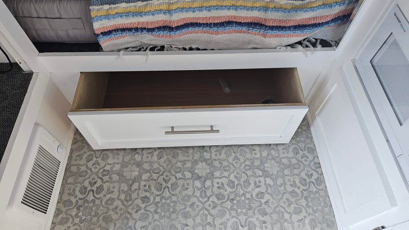 RV rental interior shows open drawer storage, microwave, patterned floor, and a cozy bedding area. — photo 9