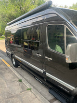 This sleek, dark Airstream Sprinter RV rental van is parked on a curb, featuring tinted windows and a roof awning.