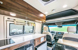 Inside a luxurious RV rental: modern kitchen with cooktop, sink, fridge, and comfortable swiveling front seats for travel.