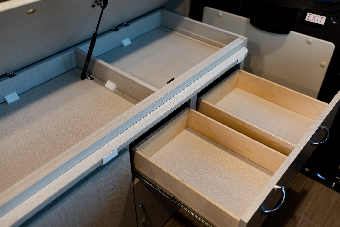 RV rental's light wood interior: An open lift-up cabinet and two pull-out drawers showcase organized storage options.