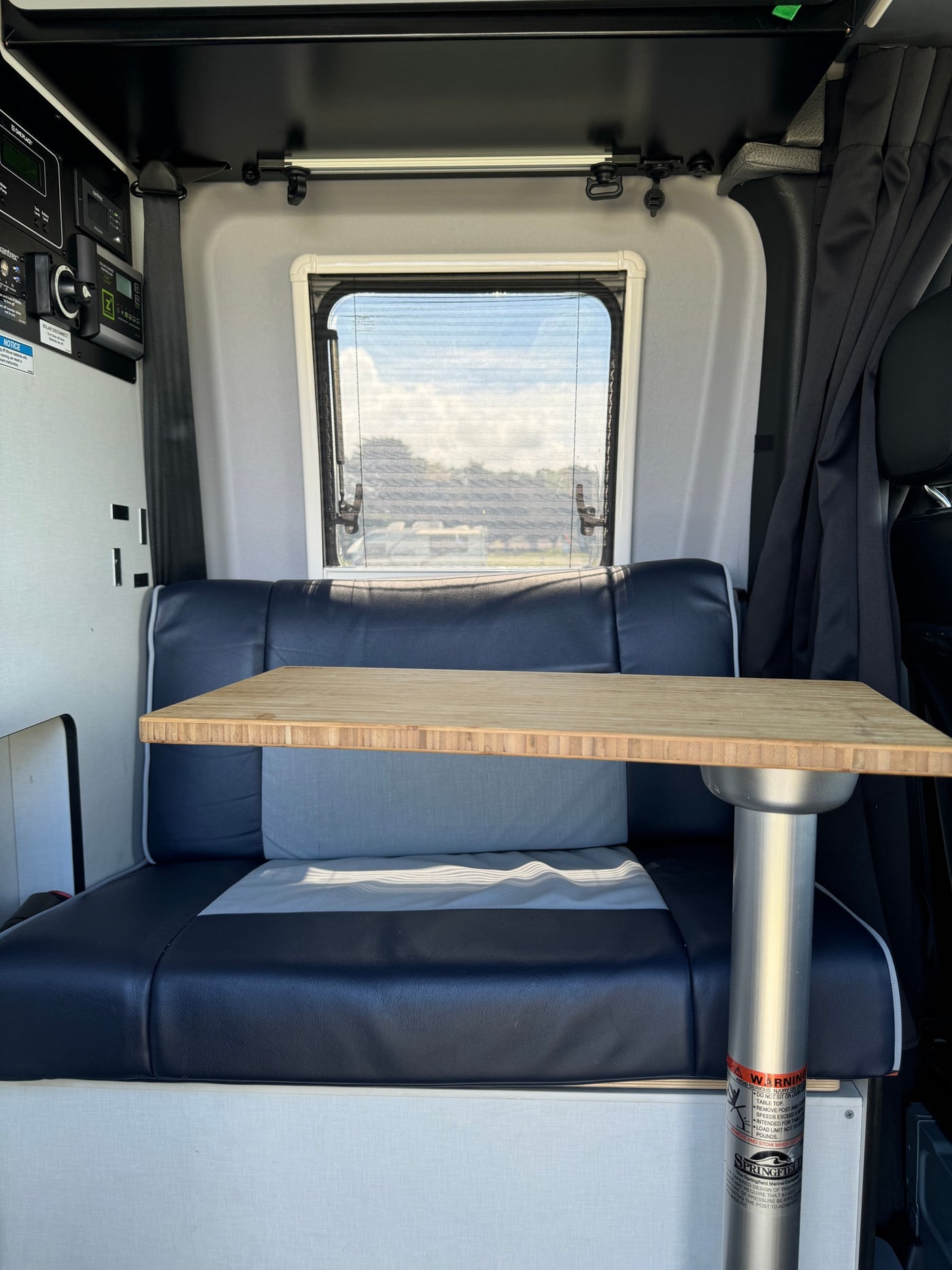 Cozy RV rental interior showing a comfortable dinette with a wooden table, window, and control panel for power management. — photo 4