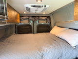 Inside an RV rental: a neatly made bed, overhead cabinets & AC. Ready for comfort on the road.