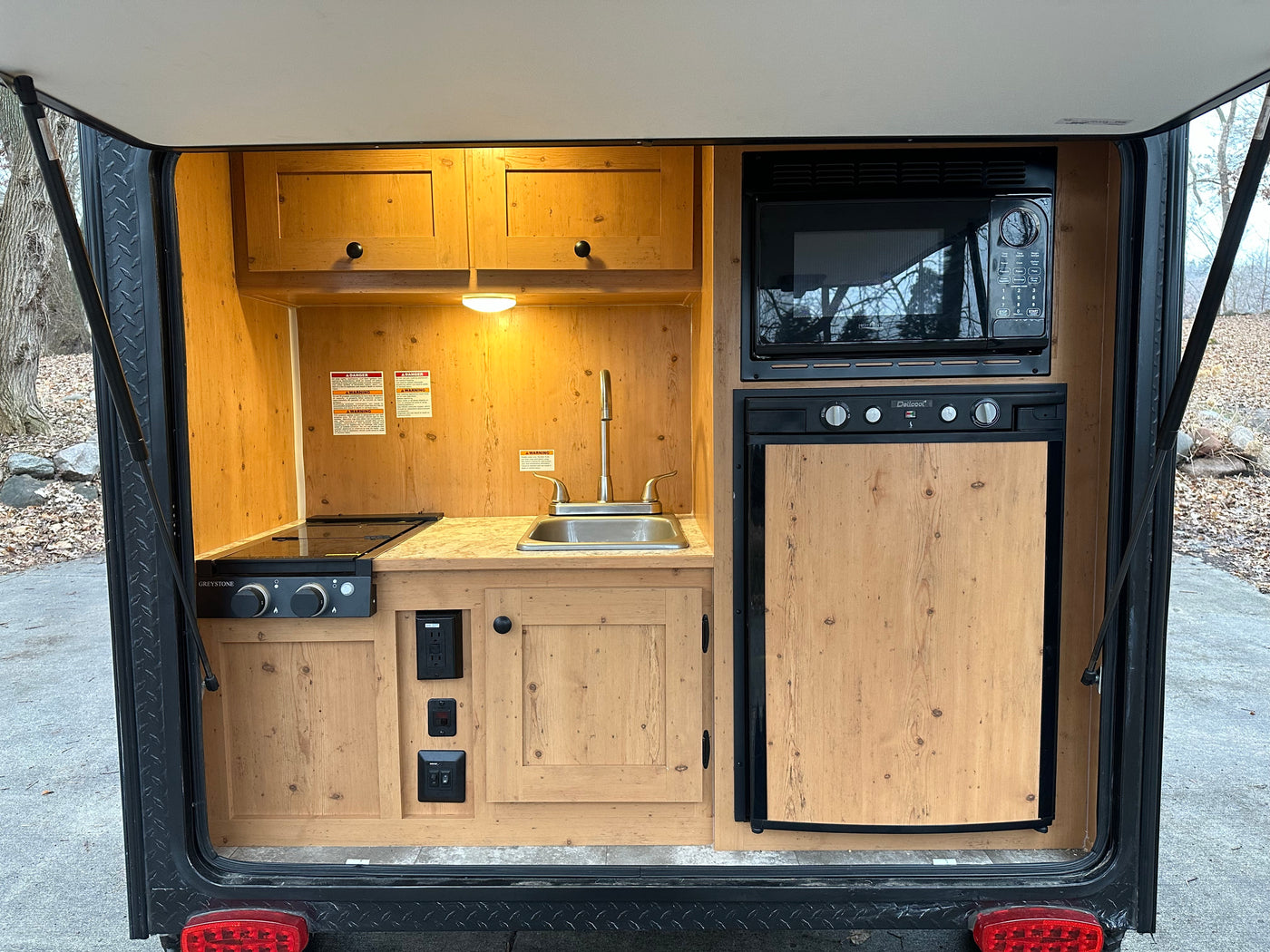 RV rental's rear outdoor kitchen: wood cabinets, sink, stovetop, microwave, & fridge for easy camping meals. — photo 4