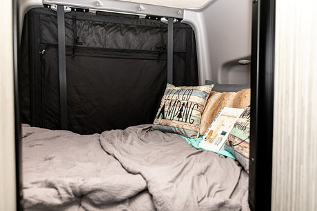 Cozy bed inside an RV rental with 'Let's Go Camping' pillows and soft blankets, ideal for comfortable travel.