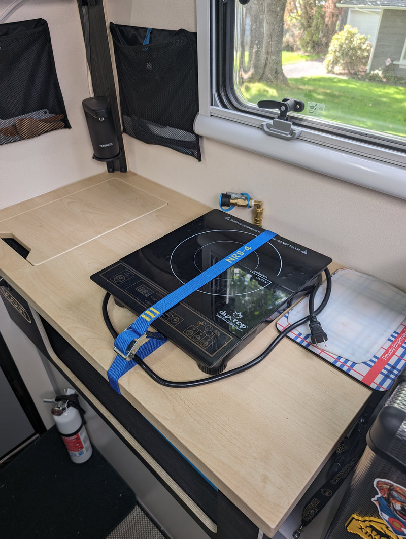 Compact rv rental kitchen area, featuring an induction cooktop secured for travel, mesh storage, and a fire extinguisher. — photo 12