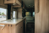 Bright, modern rv rental interior: kitchen with sink and counter, leading to a comfortable rear living area.