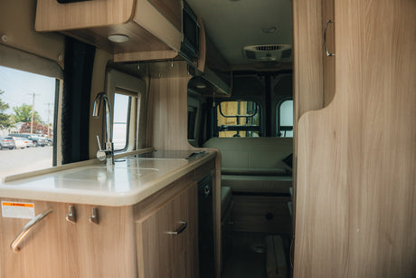 Bright, modern rv rental interior: kitchen with sink and counter, leading to a comfortable rear living area.