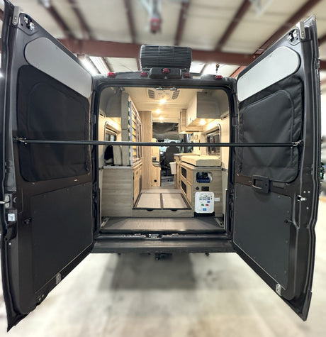 Rear view of an RV rental camper van with open doors, revealing its spacious, customized interior and comfortable amenities.