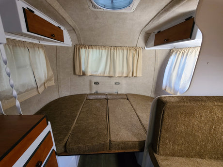 Cozy RV rental interior featuring a convertible bed/seating area, overhead storage, and privacy curtains.