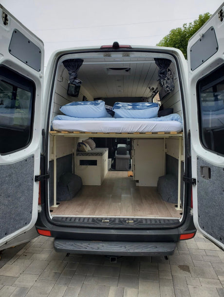 RV rental: Camper van interior from the back, showing a raised bed, under-bed storage, and wood plank floor.