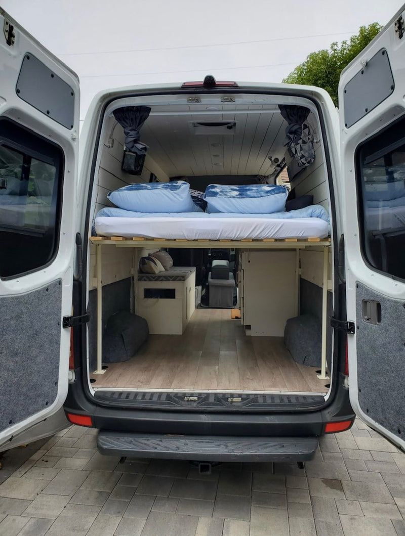 RV rental: Camper van interior from the back, showing a raised bed, under-bed storage, and wood plank floor. — photo 16