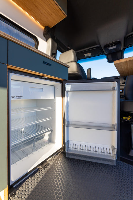Clean RV rental interior showing an open, empty refrigerator with shelves. Modern design, ready for your travel essentials.