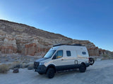RV rental van, cream-colored, parked at unique desert rock formations under a clear sky, ready for your next adventure.