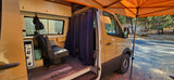 RV rental with side door open, revealing a cozy van interior, parked under an orange canopy for camping.