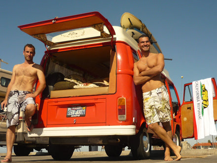 Two men and a vintage red California camper van, equipped with surfboards. Your next RV rental for beach adventures!