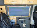 Custom RV rental interior featuring a passenger seat, overhead cabinets, window blind, and a Lagun table mount.