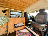 Cozy RV rental interior with wood-paneled ceiling, custom kitchen, bed, and Dometic cooler for your next adventure.