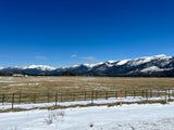 Snowy mountains frame a vast field, melting snow, and a fence under a blue sky. Perfect for an RV rental trip.