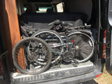 Two folding bicycles stored in an RV rental van's rear, on a protective quilted blanket.