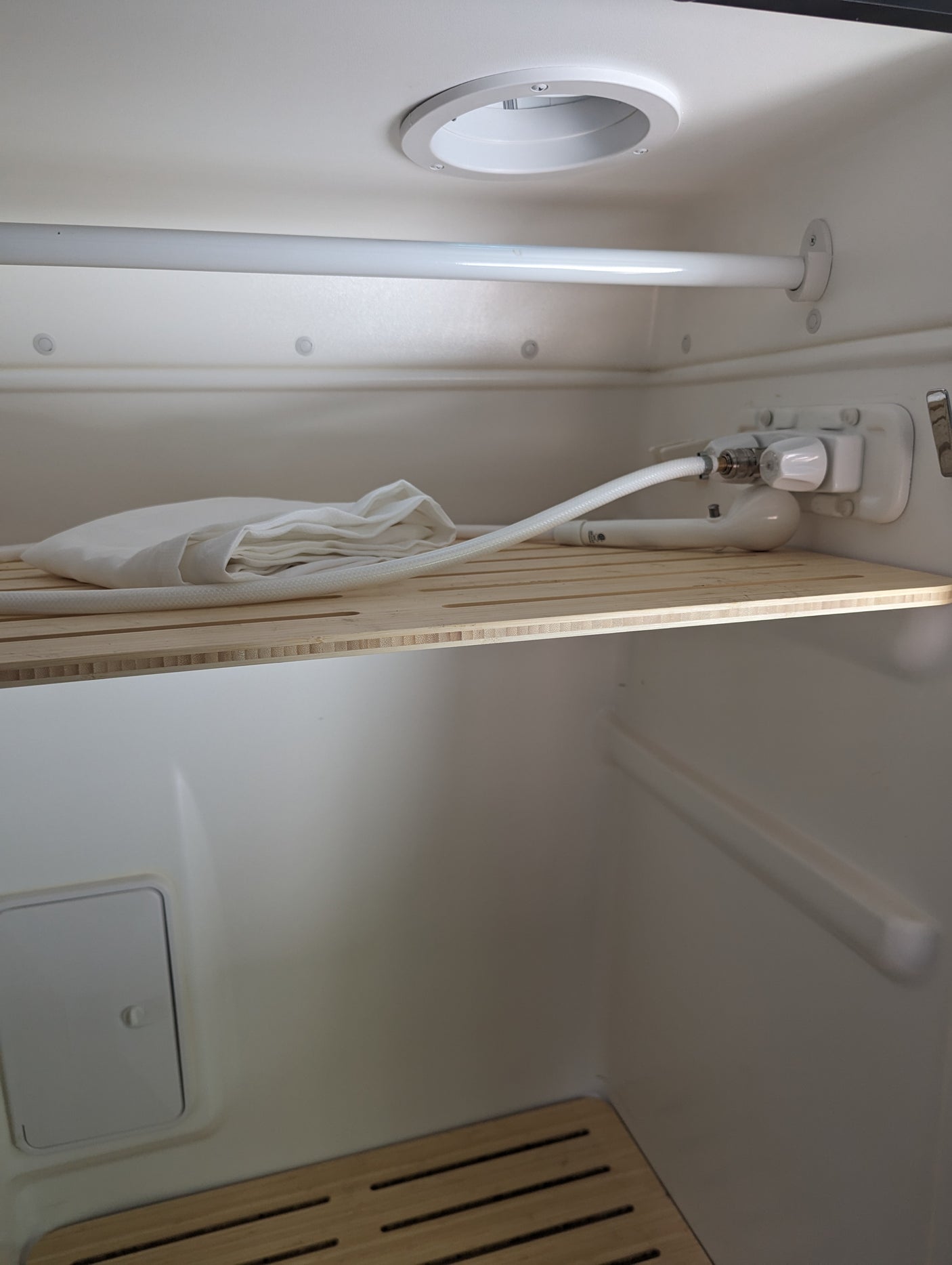 rv rental compact wet bath interior, showing shower controls, hose, white towel, and slatted wooden shelf.