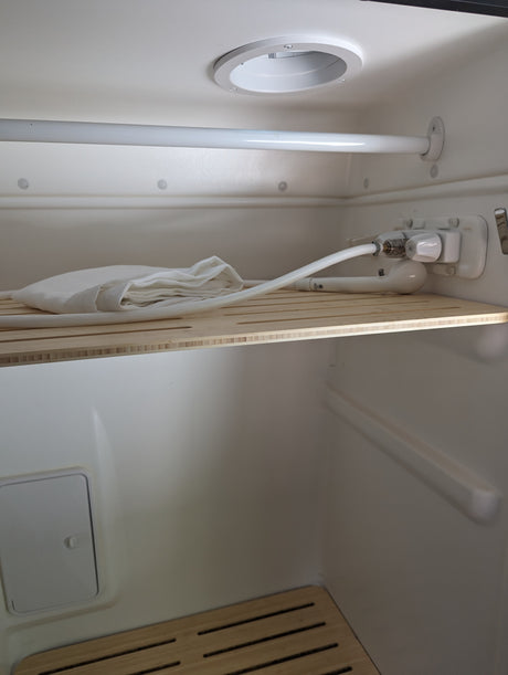 rv rental compact wet bath interior, showing shower controls, hose, white towel, and slatted wooden shelf.