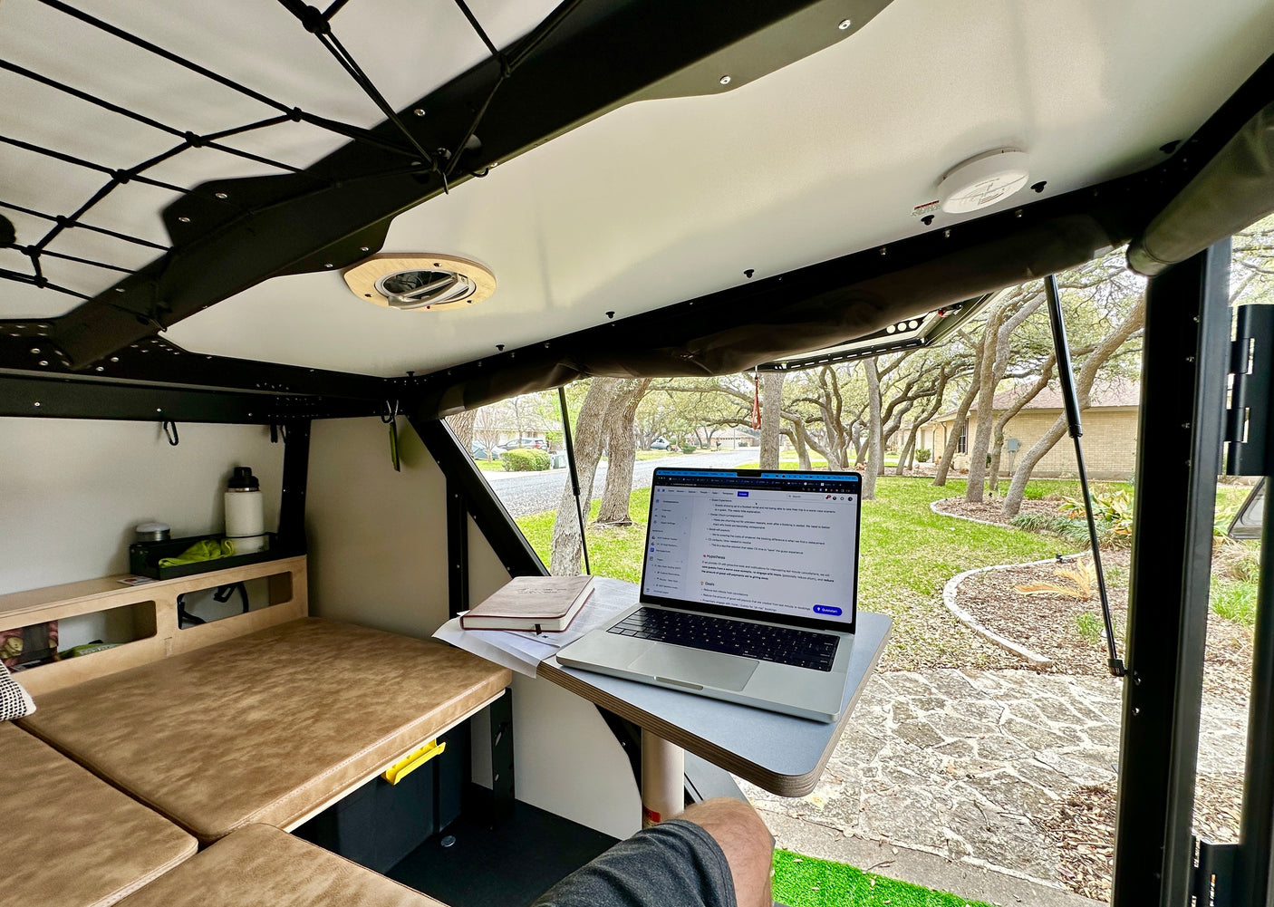 Working from a comfortable RV rental: A laptop and desk set up inside a compact camper with a view of a treelined neighborhood.