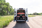 This custom RV rental camper van features dual bunk beds, seen with its back doors open on a gravel road, inviting adventure.