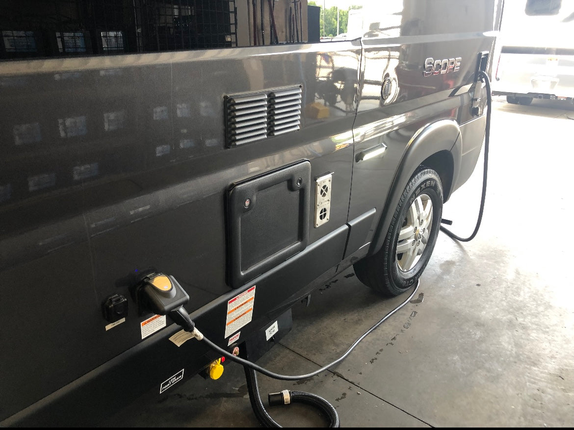 Side view of a grey RV rental (camper van) with electrical shore power, water inlets, and utility access panels clearly visible.