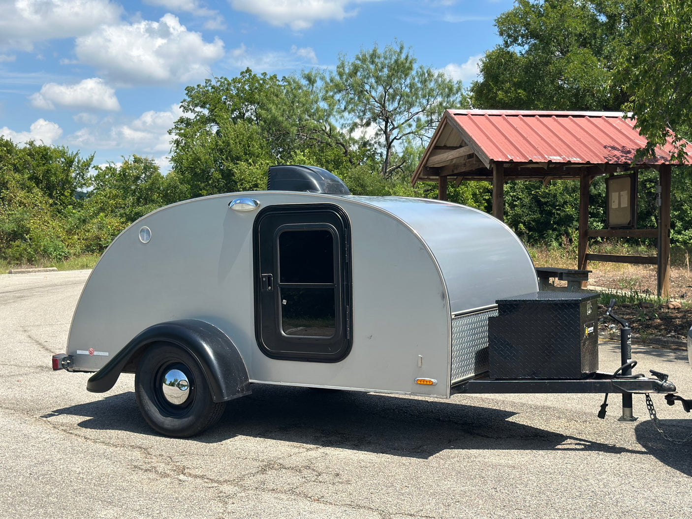 Silver teardrop camper for rv rental parked outdoors, ready for travel. Ideal for a compact camping adventure.