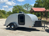 Silver teardrop camper for rv rental parked outdoors, ready for travel. Ideal for a compact camping adventure.