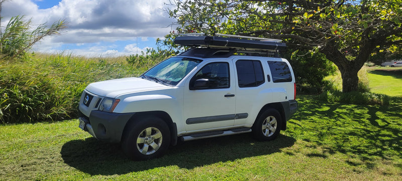 White Nissan Xterra SUV with a rooftop tent parked on grass, offering a compact outdoor vehicle for RV rental adventures. — photo 3