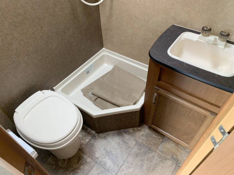 This RV rental features a compact bathroom with a toilet, sink vanity, and corner shower pan for your travels.