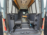 Step into this spacious RV rental camper van interior, featuring rear-facing bench seating, a dining table, overhead cabinets, and practical storage.