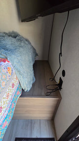 RV rental bedroom view: a mounted TV above a bed with a plush blue blanket & quilt, next to a shelf with cables.