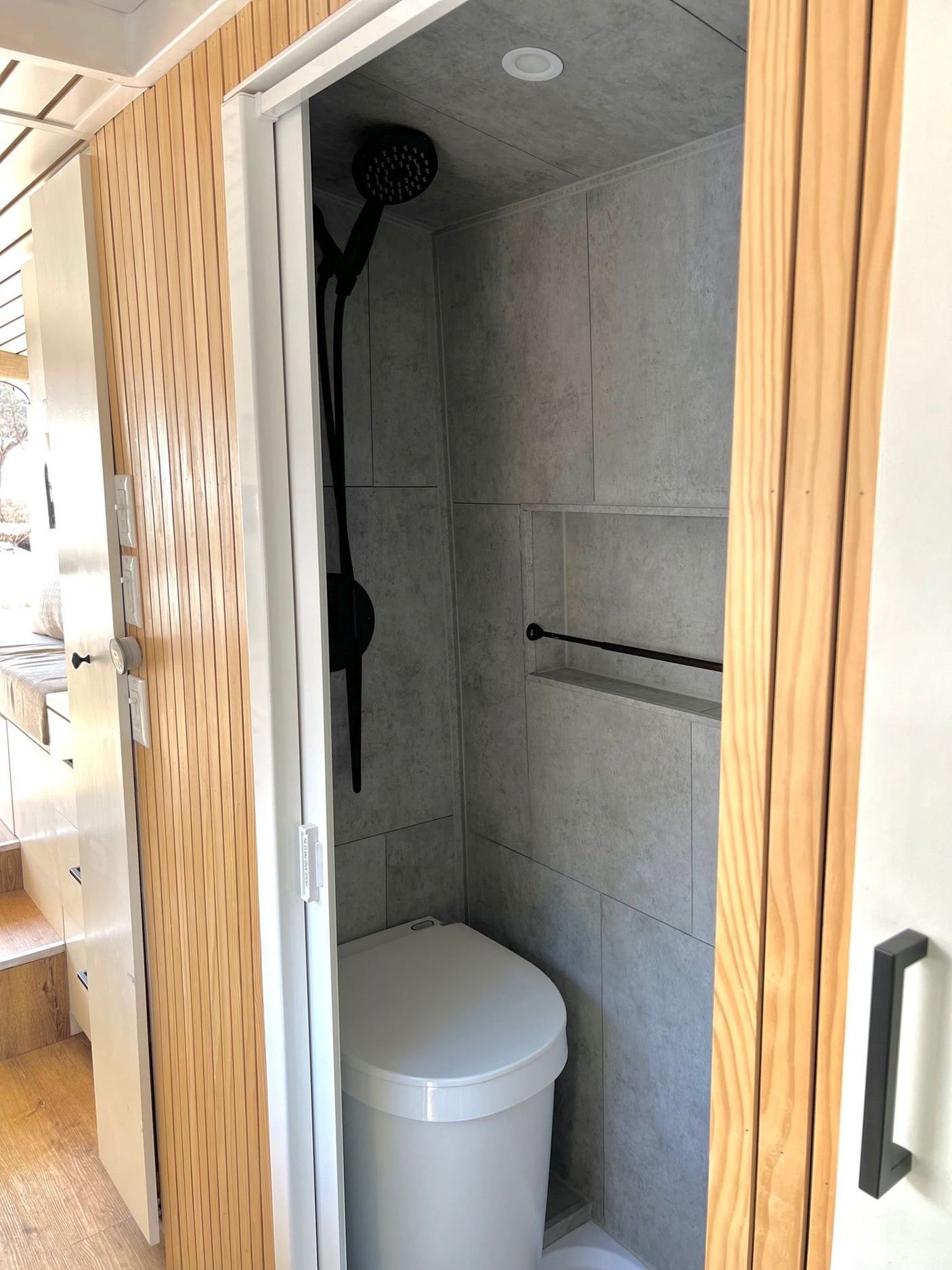 Compact RV rental bathroom showcasing a tiled shower with a black showerhead, white toilet, and recessed shelf.
