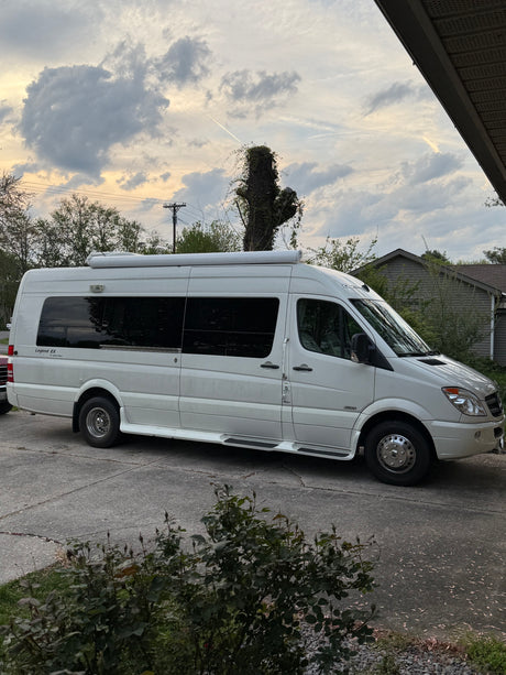White Mercedes-Benz Sprinter RV rental parked on a concrete driveway, ready for adventure under a cloudy sky.