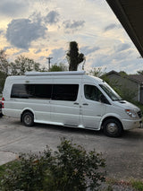 White Mercedes-Benz Sprinter RV rental parked on a concrete driveway, ready for adventure under a cloudy sky.