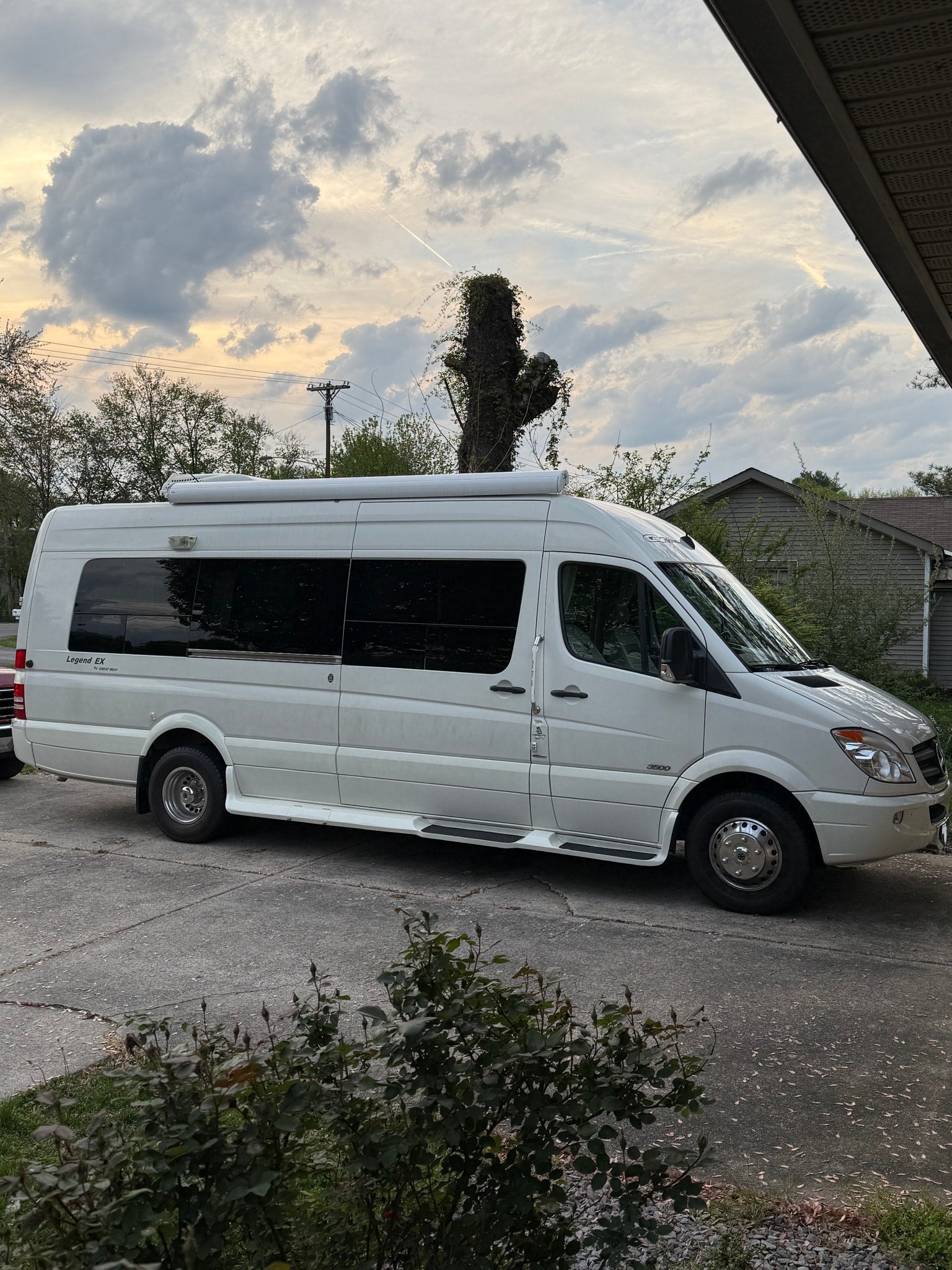 White Mercedes-Benz Sprinter RV rental parked on a concrete driveway, ready for adventure under a cloudy sky.