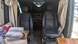 Interior of an RV rental: swiveling front seats, dashboard, side curtains, and a glimpse of the cozy living area with blankets.