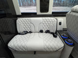 Luxury RV rental interior showcasing white diamond-quilted bench seating with seatbelts and blue illuminated cupholders.
