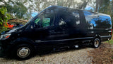 Stylish black Sprinter camper van, ready for rv rental, parked on gravel with trees reflecting.