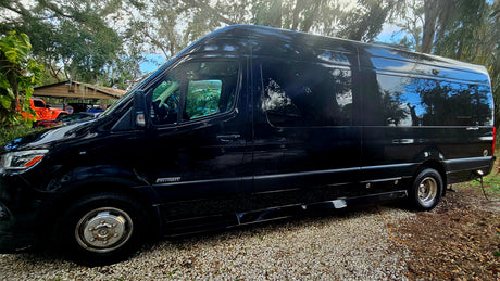 Stylish black Sprinter camper van, ready for rv rental, parked on gravel with trees reflecting.