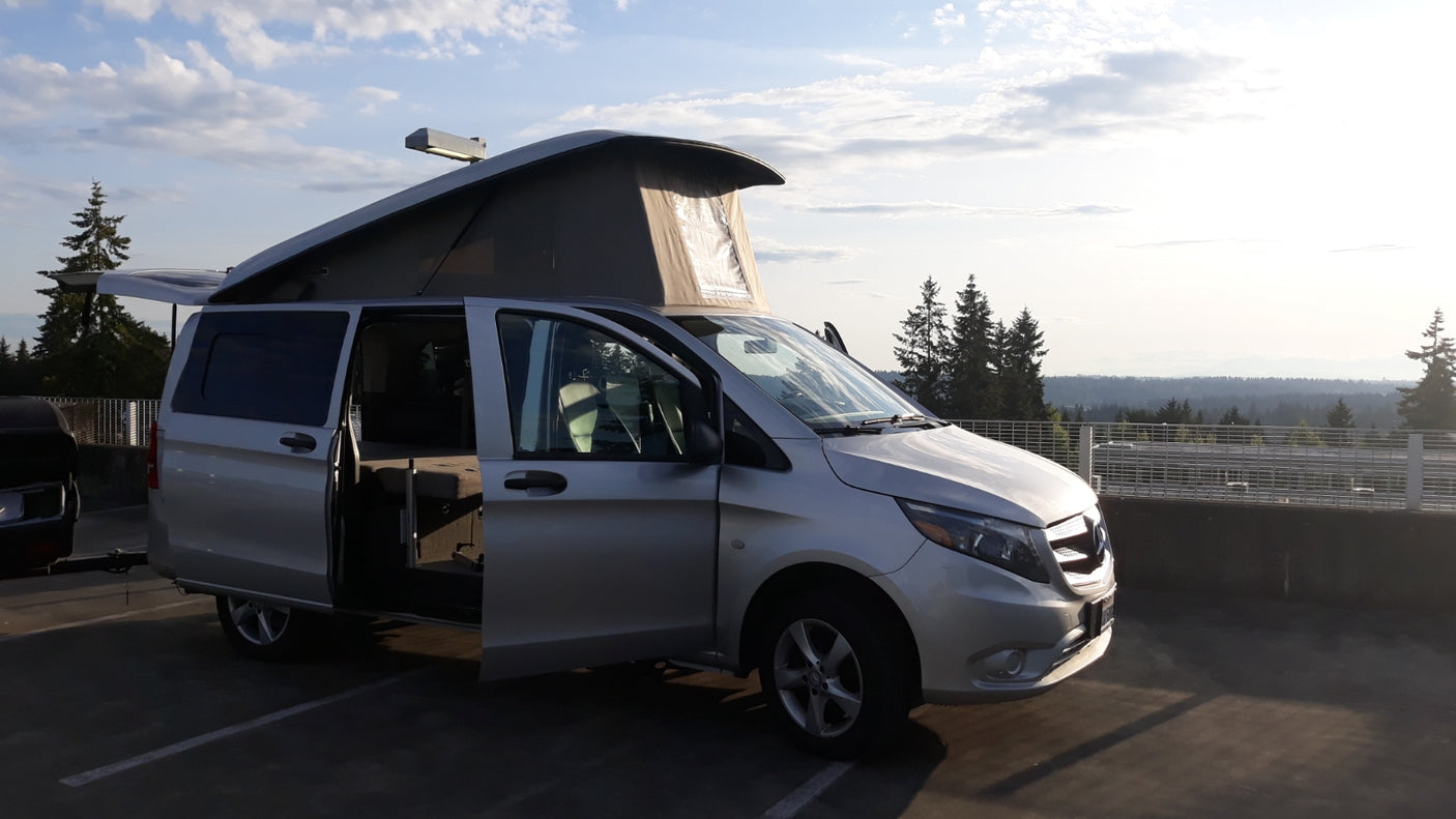 Silver pop-top camper van RV rental with doors open, parked on a scenic overlook.