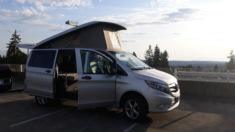 Silver pop-top camper van RV rental with doors open, parked on a scenic overlook.