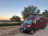 Red Winnebago Solis camper van rv rental at sunset, parked near a vineyard. Ideal for a scenic road trip.