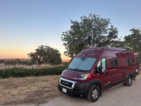 Red Winnebago Solis camper van rv rental at sunset, parked near a vineyard. Ideal for a scenic road trip.