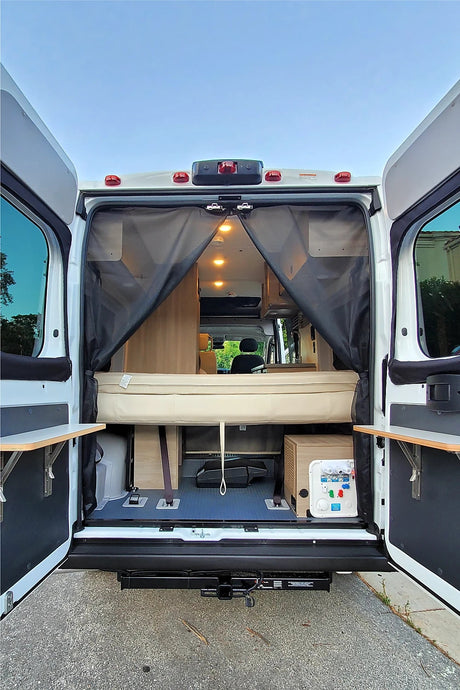 Open RV rental rear view: a cozy bed, accessible storage, and utility panel visible through wide-open doors.