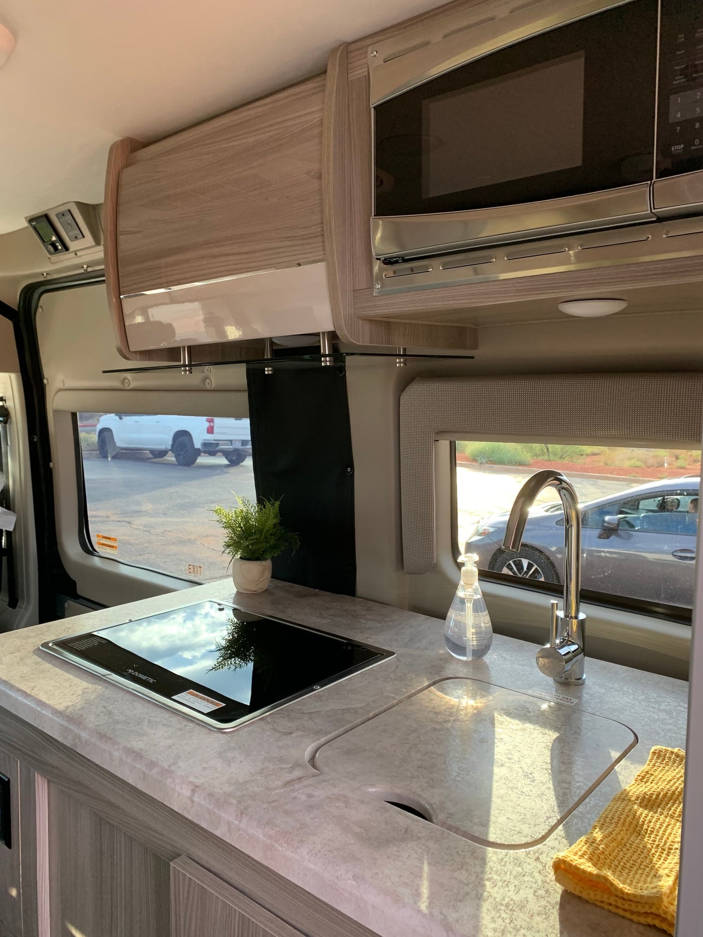 Compact RV rental kitchen area featuring a cooktop, sink with faucet, microwave, and overhead cabinets. — photo 9