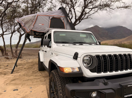 White Jeep Wrangler with a Roofnest rooftop tent set up for adventure camping. An ideal rv rental for exploring rugged terrain.